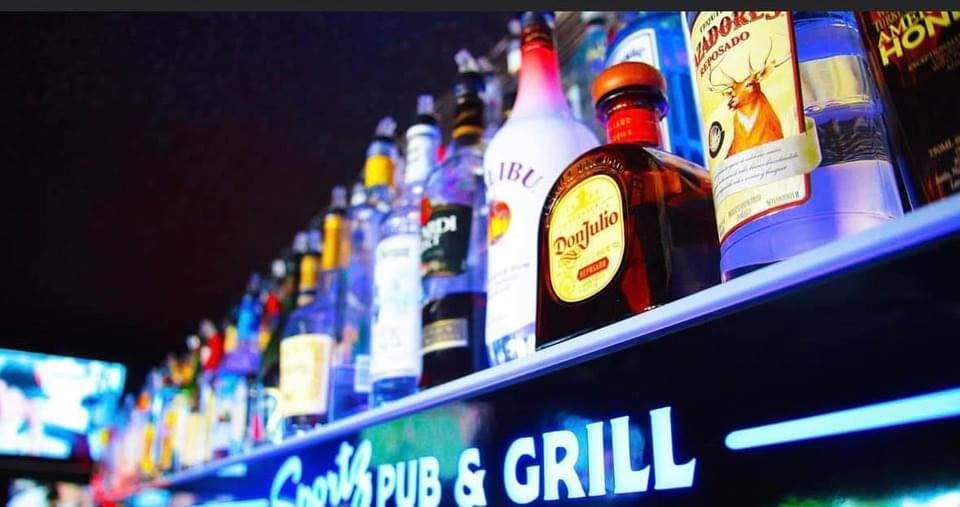 The back bar lit in blue neon, bottles lined up under the Sportz Pub & Grill sign