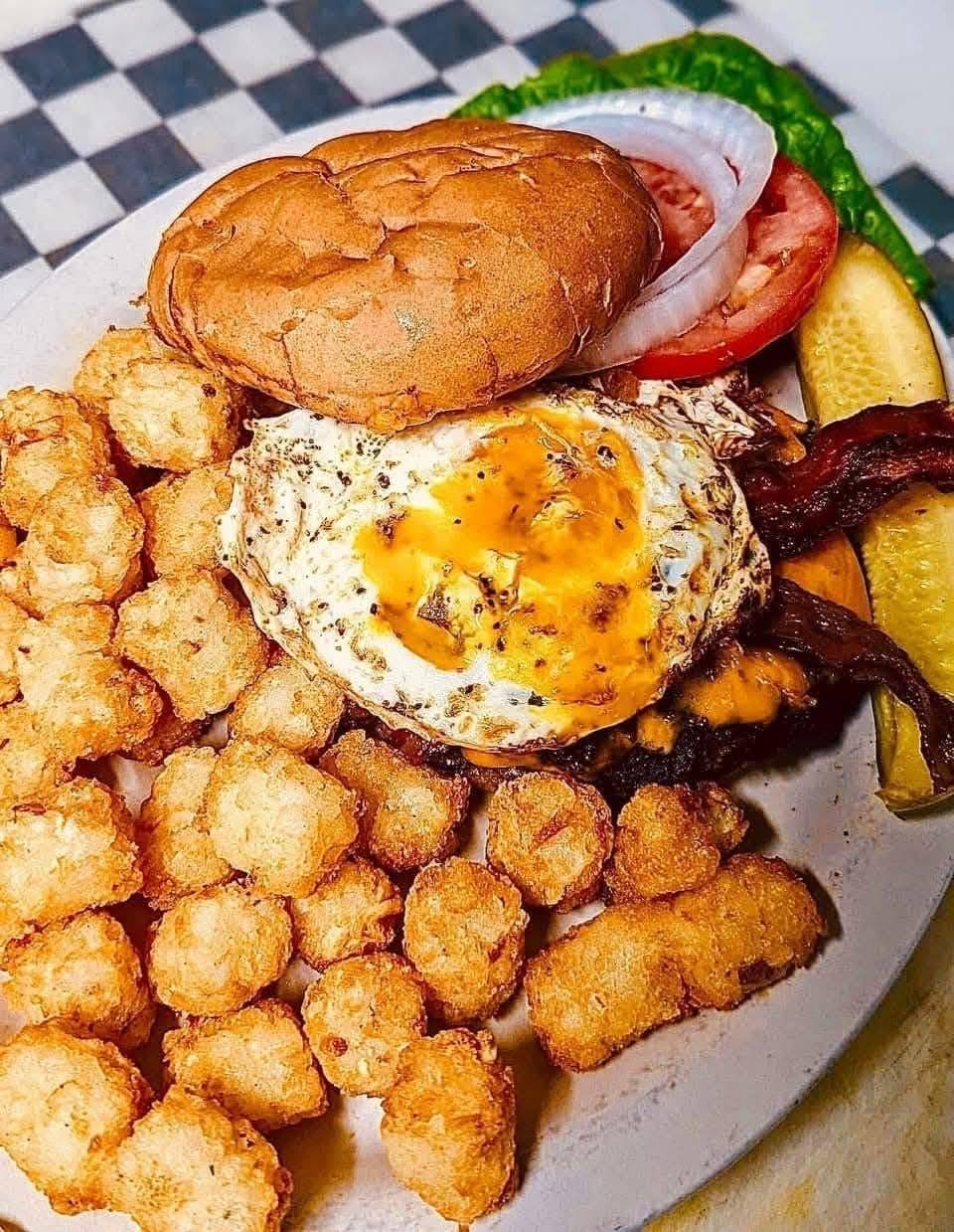 A burger topped with a fried egg and bacon, with tater tots