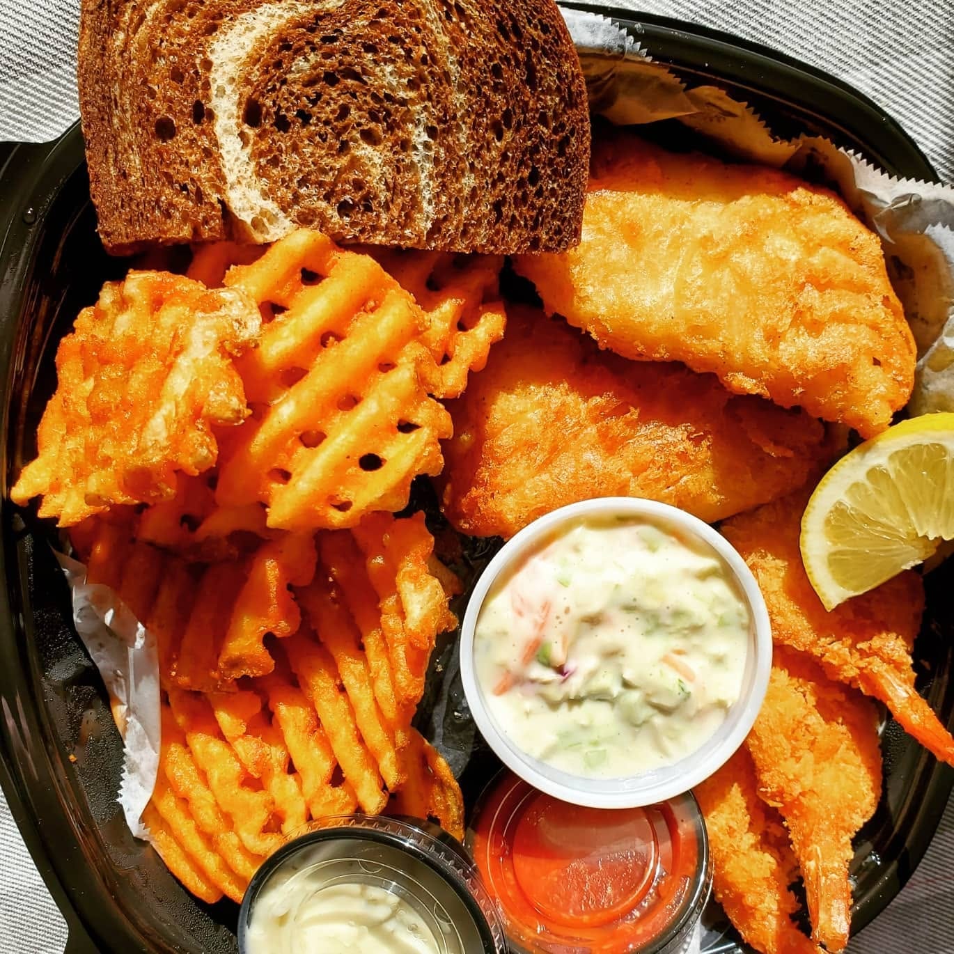 A fish fry basket: golden battered fish and shrimp, waffle fries, coleslaw, tartar sauce, lemon and rye bread