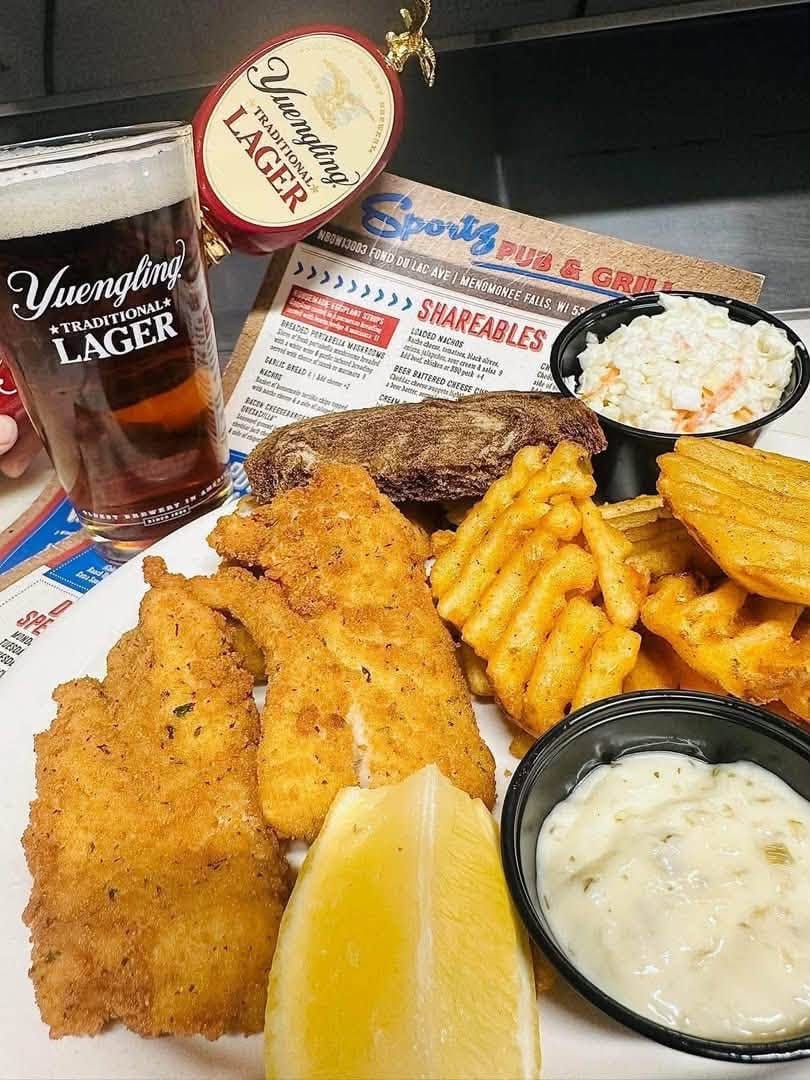 Breaded fish with waffle fries, coleslaw, tartar and lemon, beside a Yuengling