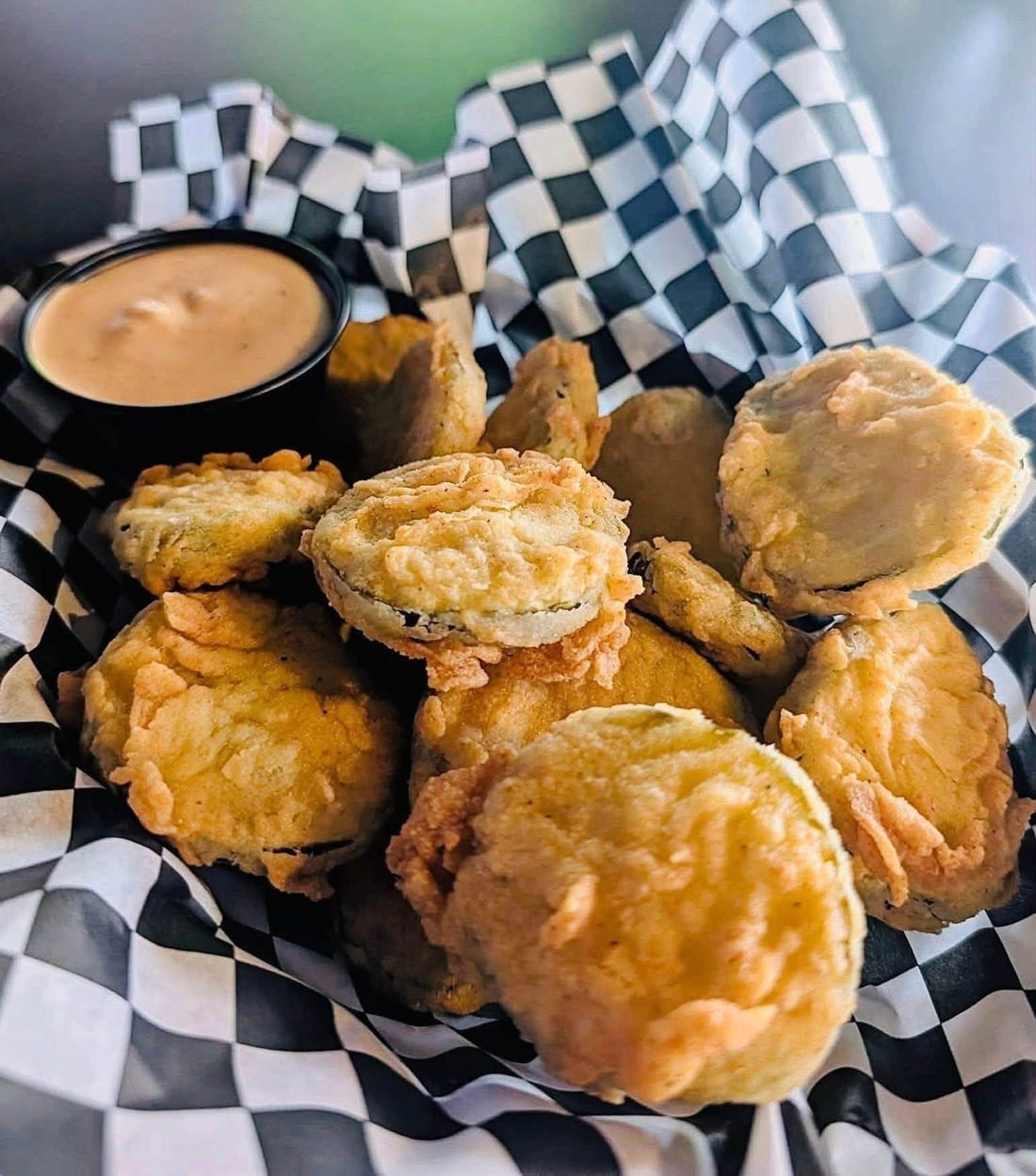 A basket of golden fried pickle chips with dipping sauce
