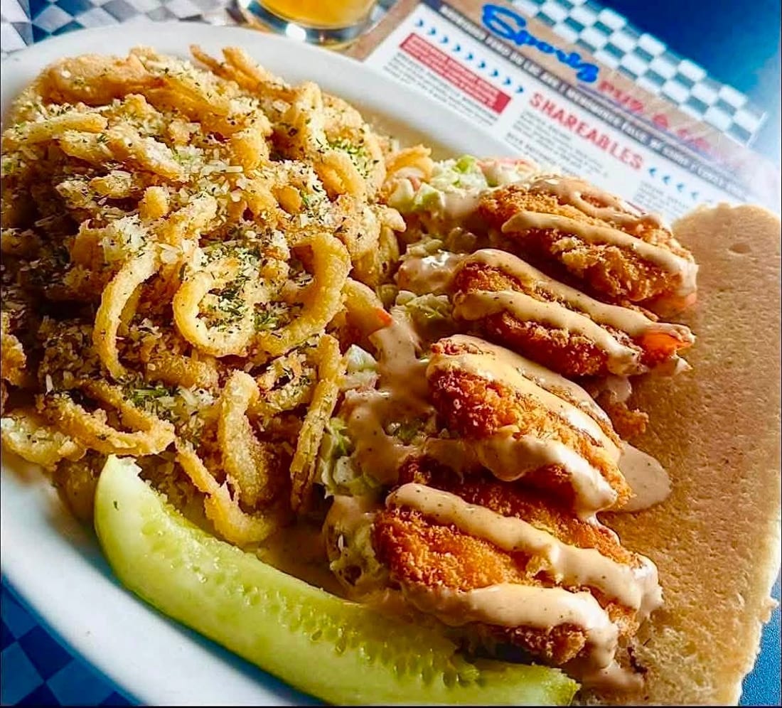 A shrimp po&rsquo; boy piled with onion strings and sauce